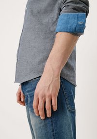 Lichtgrijs overhemd met knopen en een contrasterende blauwe denim manchet, gecombineerd met vervaagde blauwe spijkerbroek, met een ontspannen pasvorm en eenvoudig ontwerp.