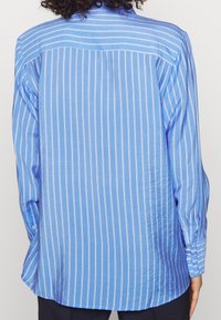 Himmelblaues Langarmhemd mit vertikalen weißen Streifen, einem Button-Down-Kragen und geknöpften Ärmeln. Glattes Material mit lässiger Passform.