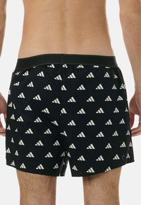 Svarta badshorts med ett upprepat vitt triangulmönster. Tillverkade av lätt tyg med en elastisk midja för komfort.