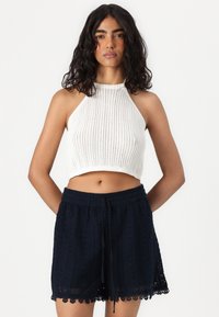 Valkoinen ribattua neuletta oleva halterneck-crop-top ja tummansiniset virkattu shortsit, joissa on aallotettu helma, säätöhihnalla ja kuvioitulla pinnalla.