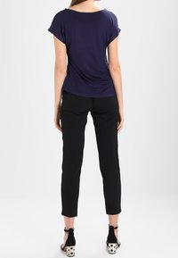 Mörkblå kortärmad topp med draperad design, kombinerad med slim-fit svarta byxor, förhöjd av blockklackssandaler i svart och vitt mönster.