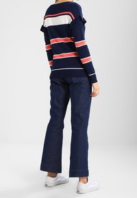 Marinrandig långärmad topp med röda och vita ränder, med volangärmar. Kommer med mörkblå denimbyxor med utsvängda ben och vita sneakers.