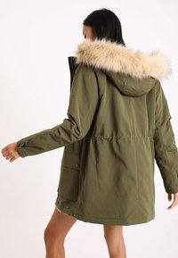 Olivově zelená parka s kapucí z umělé kožešiny, opatřená předním zipem, elastickým pasem a bočními kapsami. Texturovaná látka s hladkým povrchem.