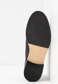 Semelle d'une chaussure noire avec l'avant et le talon texturés, section médiane lisse couleur fauve, et numéro de taille 37 marqué au centre.