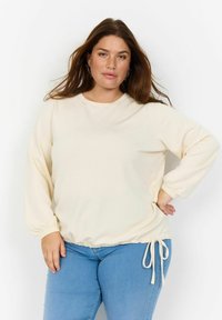Ljus beige långärmad sweatshirt med rund halsringning och elastiska cuffar. Har en rynkad midja med en knytdetalj.