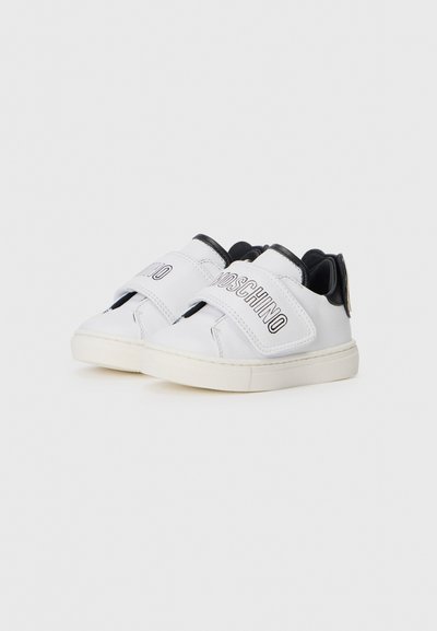 White leather sneakers with black accents, Velcro straps, and a textured white sole. Features Moschino branding in black on the strap.
