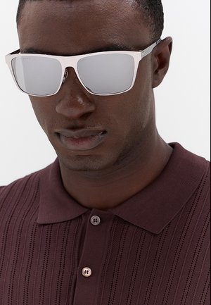 Uomo che indossa occhiali da sole argento riflettenti e una polo bordeaux scuro con texture, colletto e bottoni.