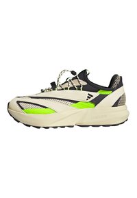 Beżowo-czarny sneaker z zielonymi akcentami, charakteryzujący się smukłym designem, panelami z siateczki i teksturowaną podeszwą. Posiada unikalny system sznurowania.