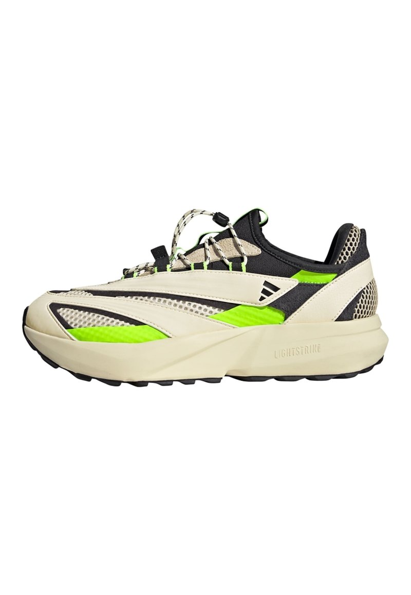 Beżowo-czarny sneaker z zielonymi akcentami, charakteryzujący się smukłym designem, panelami z siateczki i teksturowaną podeszwą. Posiada unikalny system sznurowania.