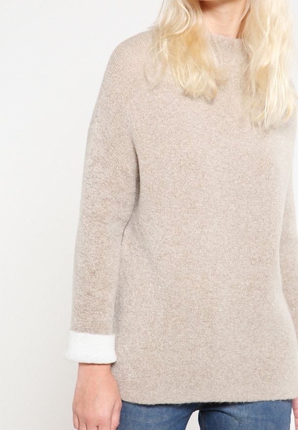 Beige Strickpullover mit lässiger Passform, ausgestattet mit einer strukturierten Oberfläche und weißen Ärmelakzenten. Das Design hat einen runden Ausschnitt und lange Ärmel.