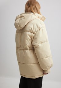 Béžová prešívaná bunda s kapucňou, s elastickým pásom a veľkými rukávmi. Hladký, ľahký materiál.