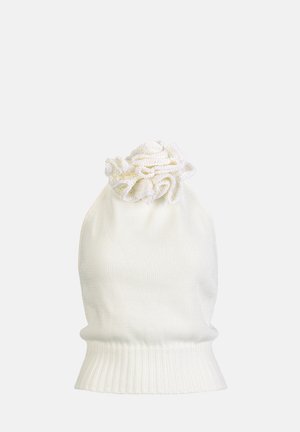 Kobieta ubrana w biały halter top z kwiatowym detalem, białe spodnie o szerokich nogawkach, brązowy pasek, brązowa kopertówka oraz beżowe sandały na obcasie.