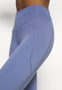 Leggings a vita alta, elasticizzati, di un colore lavanda tenue. Texture liscia con cuciture piatte e dettagli di design sottili sui lati.