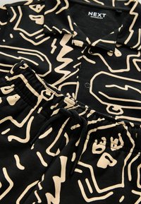 Ensemble chemise et shorts noirs avec motifs abstraits de visages beiges et shorts à taille élastique, montrant l'étiquette de la marque NEXT sur le col.