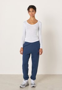 Valge pika varrukaga särk sügava V-kaelusega, kombineeritud tumesiniste dressipükstega, millel on elastne vöökoht ja soonikkoes mansetid. Hallid vabaajajalatsid.