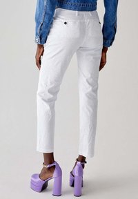 Pantaloni bianchi a fantasia con taglio dritto, abbinati a tacchi a piattaforma viola. L'outfit presenta una giacca di jeans con cuciture visibili.