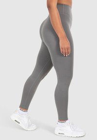 Leggings grigi alti in vita realizzati in tessuto elasticizzato, con una superficie liscia e cuciture a contrasto, abbinati a sneaker bianche.