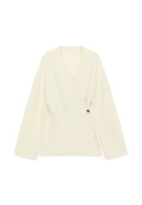 Pull enveloppant de couleur crème en maille douce. Présente un décolleté en V profond, des manches larges et un détail décoratif avec un bouton.