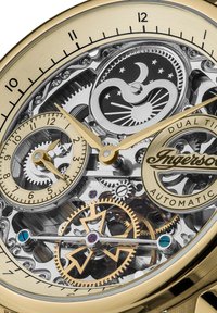 Montre dorée avec un cadran squelettique transparent ; présente des engrenages complexes, des affichages de l'heure double et un logo en bas.