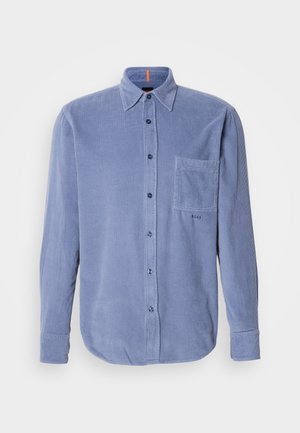 Blaue Corduroy-Hemdjacke mit einer Tasche auf der linken Brust, langen Ärmeln und abgerundetem Saum. Der Stoff hat eine gerippte Textur.