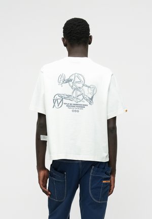 Valkoinen puuvillapaita, jossa on graafinen printti selässä. Printissä on toisiinsa liittyviä muotoja ja teksti "REPLAY INC ENGINEERED WORKS". Lyhyet hihat.