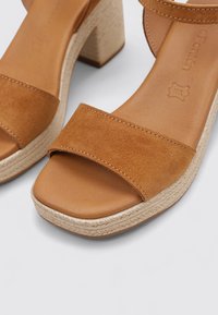 Sandalias de ante marrón con tiras y punta cuadrada, una plataforma de yute texturizada y un tacón sólido. Plantilla de piel suave.