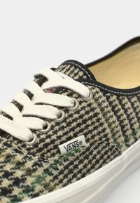 Vans sneakers met een geweven zwart, groen en beige patroon, met crèmekleurige veters en een witte logo-tag, afgewerkt met een zwarte rand en een rubberen zool.