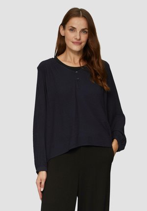 Marineblauwe langwerpige shirt in gestructureerde stof, met een gebogen zoom, ronde halslijn en een twee-knops sluiting aan de voorkant.
