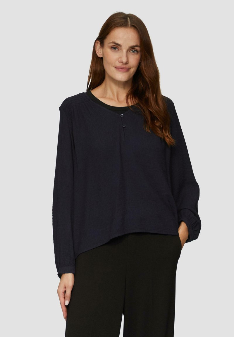 Marineblauwe langwerpige shirt in gestructureerde stof, met een gebogen zoom, ronde halslijn en een twee-knops sluiting aan de voorkant.