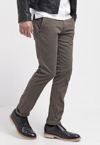 Braune Baumwollchinos mit slim Fit, ausgestattet mit Vordertaschen, kombiniert mit schwarzen Leder-Schnürschuhen und einer schwarzen Lederjacke.