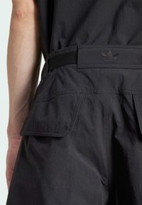 Čierne šortky s hladkou textúrou, vybavené širokým pásom s čiernym logom a dvoma postrannými vreckami. Sú viditeľné jemné švy.