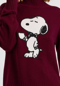 Burgunderfarbener Pullover mit einer großen, gestickten Snoopy-Grafik in Weiß und Schwarz, mit einem gerippten Rollkragen und Bündchen.