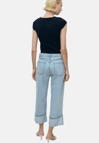 Navy short-sleeve top paired with light blue wide-leg jeans featuring rolled cuffs, five pockets, and a mid-rise fit.