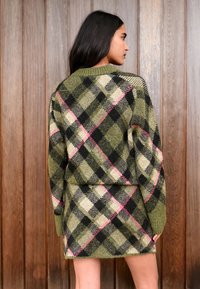 Green plaid knit sweater and skirt set, featuring pink and black accents, with a relaxed fit and ribbed collar, against a wood background.