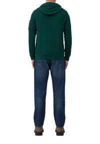 Groene gestructureerde hoodie met capuchon, lange mouwen en een ritszak op de linkerarm, gecombineerd met blauwe denim jeans.