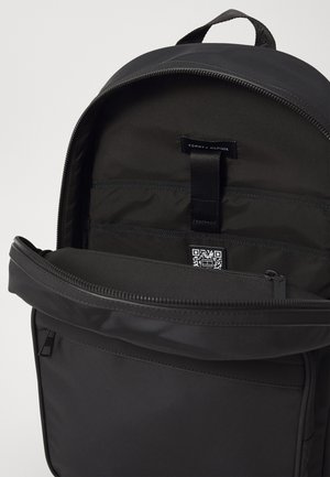 Sac à dos noir avec le compartiment principal ouvert, comprenant des poches d'organisation internes, une boucle en tissu et un code QR visible à l'intérieur.