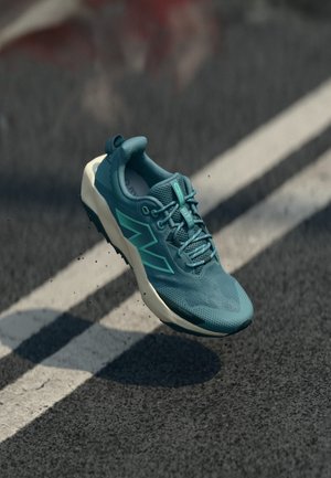 Teal športni čevelj z zgornjim delom iz teksturiranega mrežastega materiala, belim gumijastim podplatom in ostrimi poudarki v obliki vzorcev. Ima vezalke in oblazinjen ovratnik.