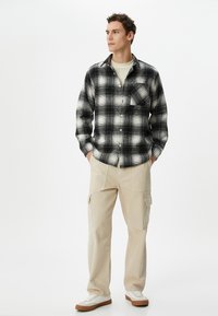 Sort og hvidternet flannel-skjorte med en frontlomme, parret med beige cargo-bukser med sidelommer. Hvide sneakers med gummisåler.