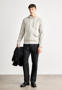 Harmaa fleece-huppari, jossa on nyörit, etutasku ja logo, yhdistettynä tummanharmaisiin suoriin farkkuihin ja mustiin kenkiin, pitäen mustaa takkia.