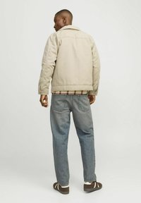 Beige, struktureret jakke med lige snit, der har krave og knaplukninger, parret med lyseblå, løstsiddende denimjeans og brune sneakers.