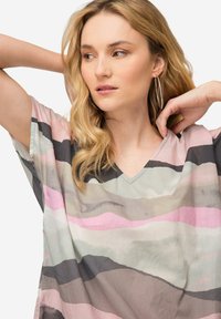 Blusa a maniche corte con scollo a V in morbido tessuto, caratterizzata da righe ondulate in rosa pastello, grigio e verde tenue, con una vestibilità rilassata e una forma fluida.