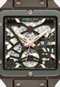 Vierkante automatische horloge met een blootgelegd uurwerk, groen en zilver ontwerp, roségouden accenten en een donker metalen kast.