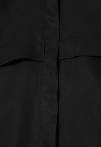 Black fabric featuring a smooth texture, with a prominent seam at the center and a folded design element near the top.