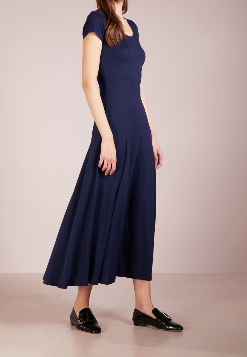 Robe bleu marine à manches courtes en tissu lisse. Jupe évasée atteignant le mollet, associée à des chaussures noires à enfiler avec boucle.