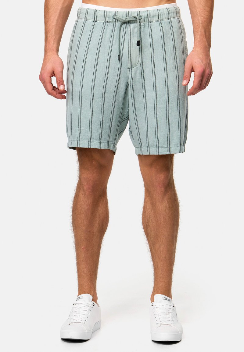 Shorts bleu clair avec des rayures noires verticales, taille élastique, fermeture à cordon et poches latérales. Portés avec des baskets blanches.