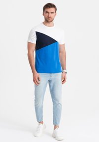 Tričko s krátkým rukávem v designu s bloky barev bílá, námořnická modrá a modrá. Spárováno s světlými modrými džíny a bílými teniskami.