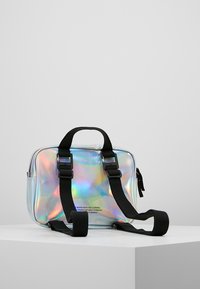 Bolsa holográfica compacta con forma rectangular, correas ajustables negras y un asa superior. Textura suave con marca en el lateral.