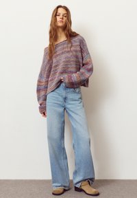 Multi-colored knitted sweater with loose fit and wide sleeves, paired with light blue wide-leg jeans and brown ankle boots.