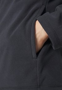 Dunkelgraue Fleecejacke mit einer Seitentasche, die eine weiche Textur und nahtlose Nähte an den Kanten aufweist.