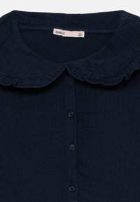 Ναυτικό μπλε μπλούζα με γιακά με βολάν, διαθέτοντας κουμπιά και υφή ύφασμα. Η ετικέτα γράφει "ONLY."